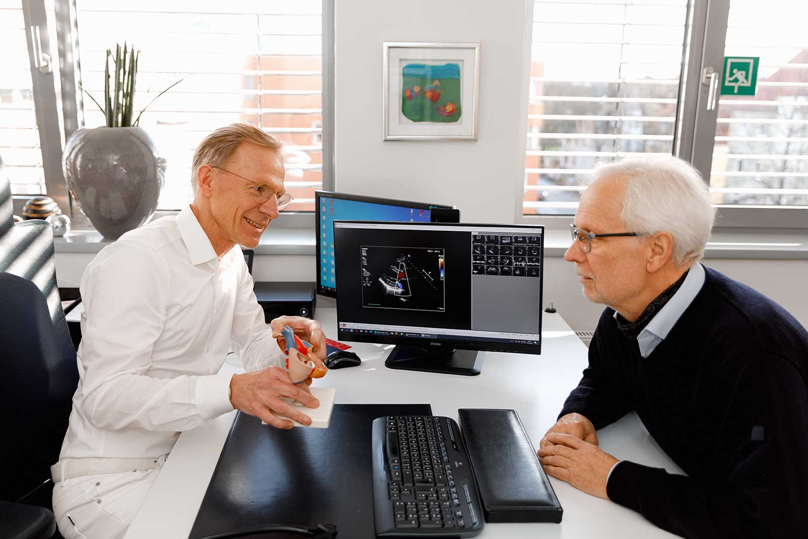 Dr. Hermes – Patientengespräch und Diagnostik im Herz- und Diabeteszentrum Osnabrück Dr. Hermes im Patientengespräch mit Herzmodell und Ultraschallbildern im Herz- und Diabeteszentrum Osnabrück